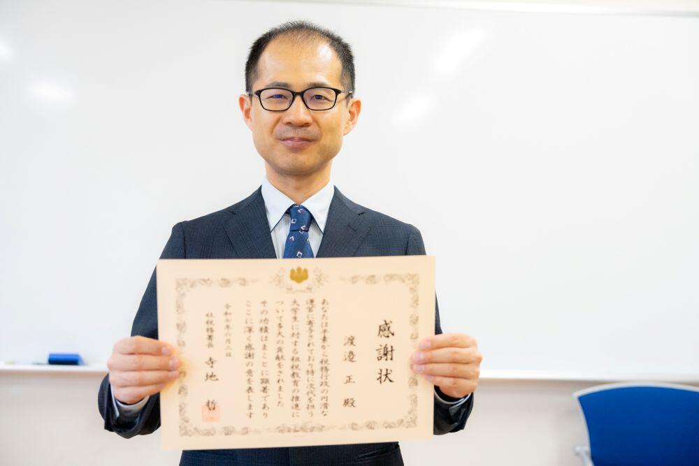 写真_表彰状をもつ渡邉正准教授